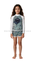 Girl wearing a long-sleeve rash guard with green ripple manta print and swim shorts