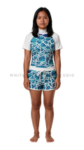 Woman in a short sleeve rash guard and shorts in the clear ocean blue Ripple print, front view